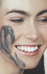 Girl with coffee scrub on her face biting the creamy face scrub tube